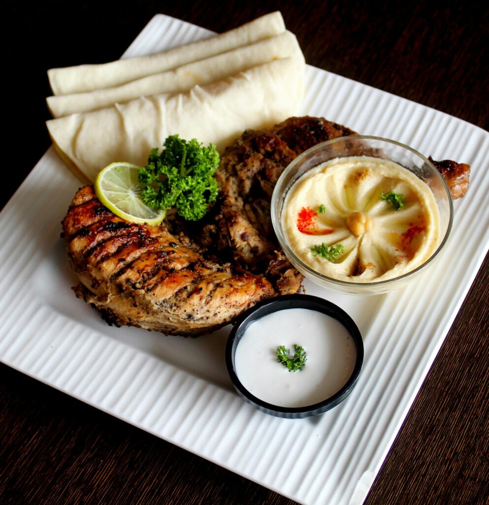 Delicious grilled chicken served with hummus and flatbreads on a square plate.