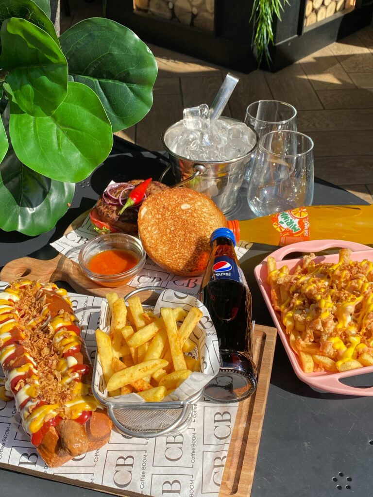A vibrant spread of fast food including hot dog, fries, and beverages at a cozy setting in Алматы, Kazakhstan.