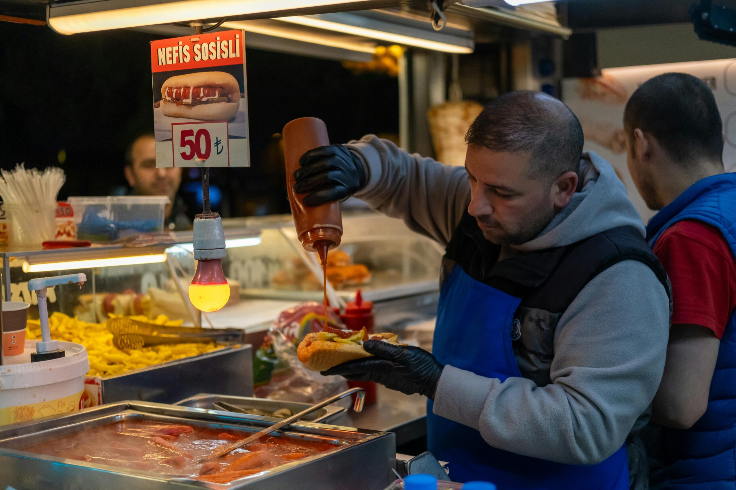 A street vendor serving hot dogs with sauce at a food stall in Istanbul, Turkey at night.