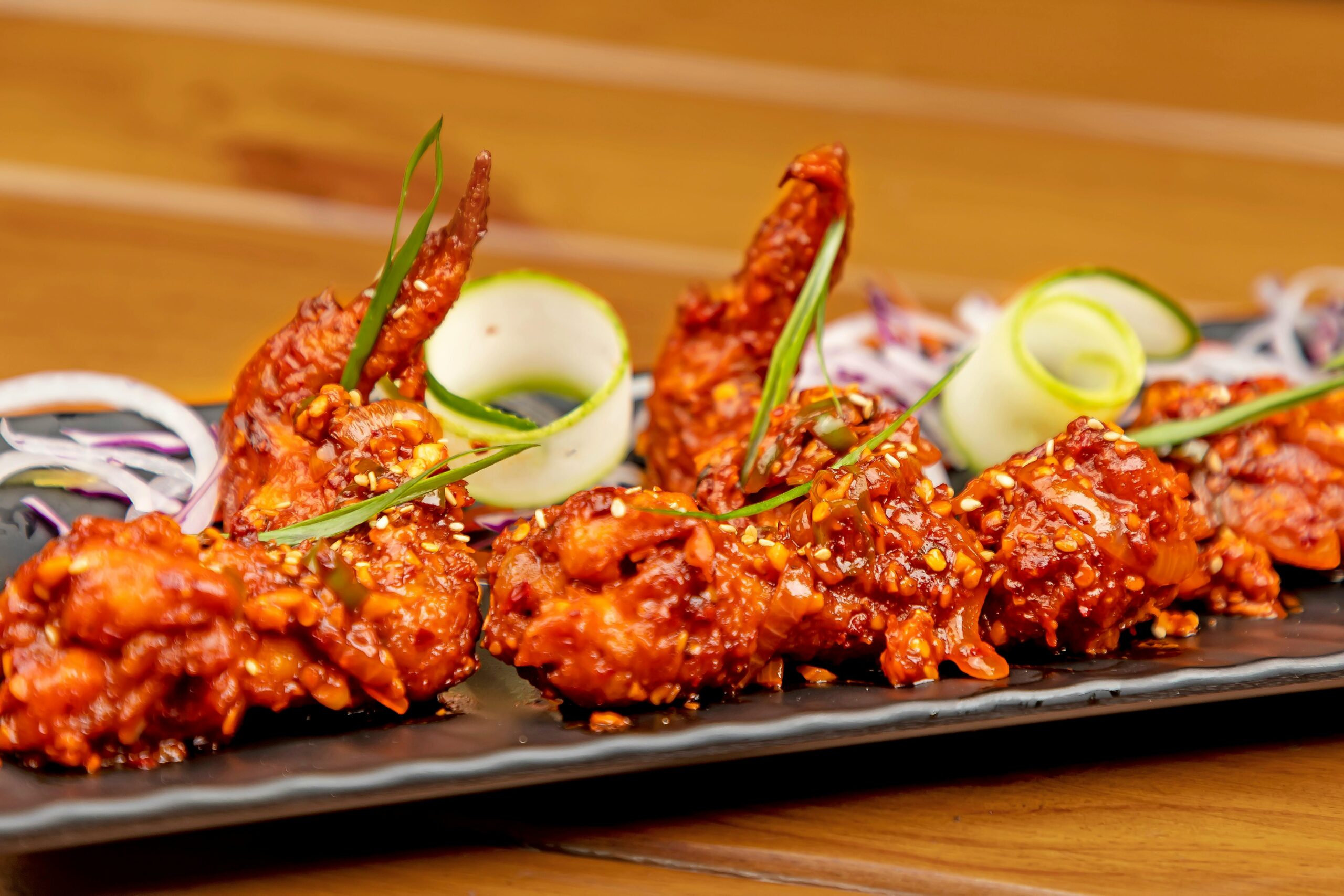 Delicious spicy glazed chicken wings garnished with sliced vegetables.