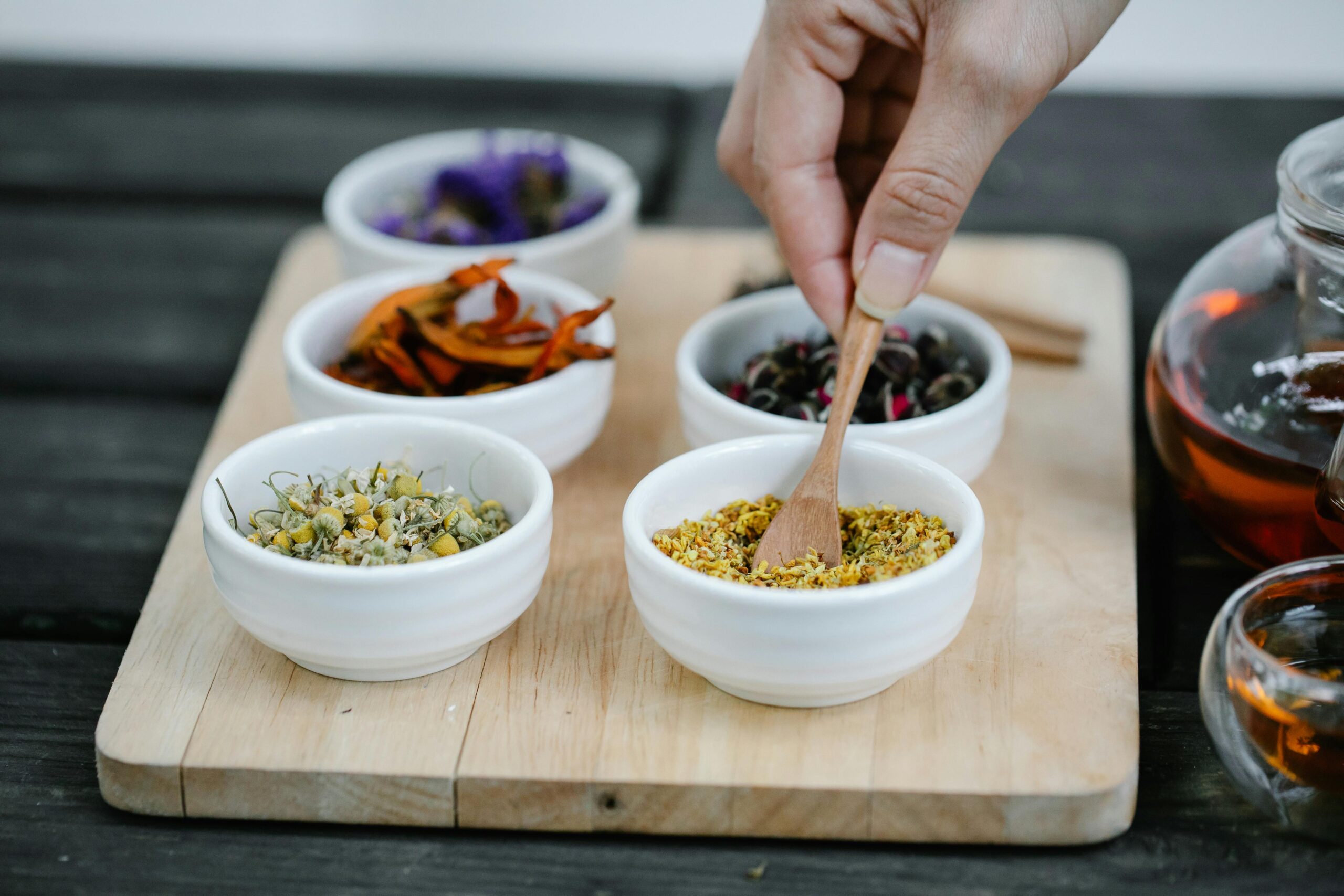 Close-up of hand choosing dried spices from bowls on a wooden tray, perfect for culinary themes.