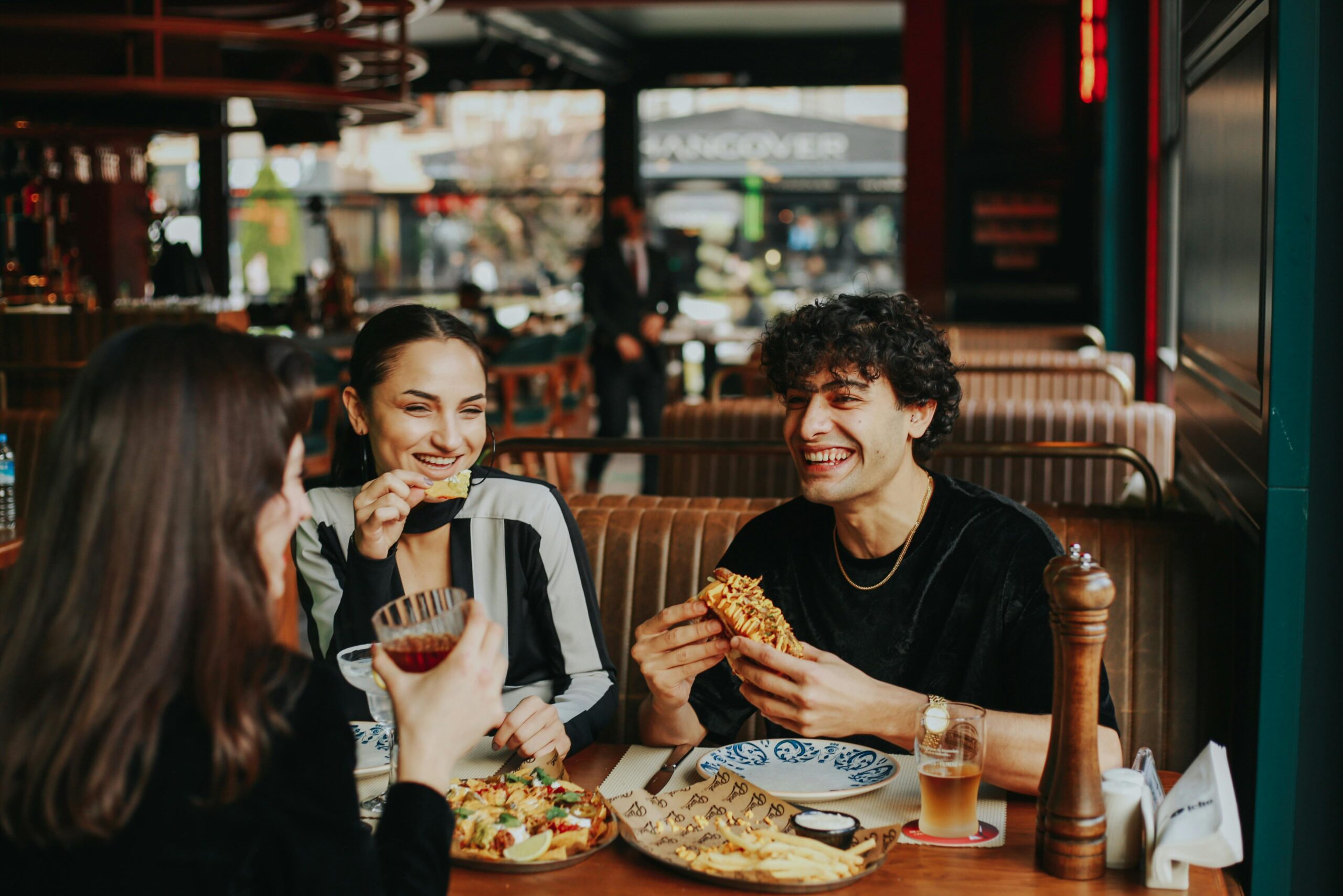 Group of friends laughing and eating at a restaurant, enjoying leisure time.